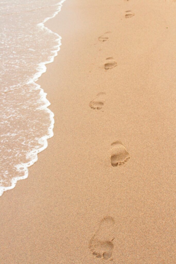 pexels-photo-2645245-2645245 Footprints on a sandy beach beside ocean waves, perfect for summer themes.